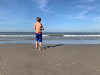 Rear view of boy on beach against sky