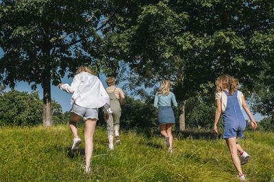 Friends running together towards trees at park