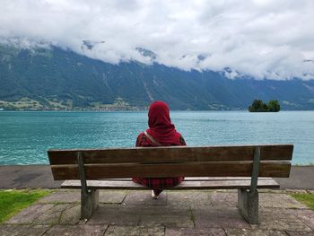 Rear view of woman sitting on bench against lake