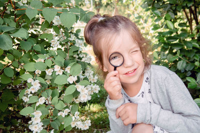 Portrait of little girl 4-7 years old with magnifying glass in examining leaves in park 