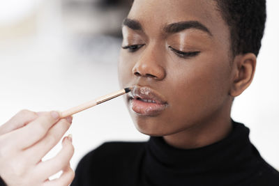 Hand of makeup artist holding brush and applying gloss on model's lips at studio
