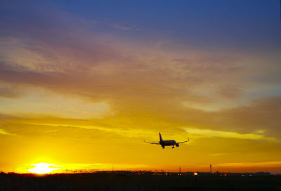 Silhouette airplane flying on sunset