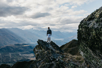 Rear view of man standing on rock against sky