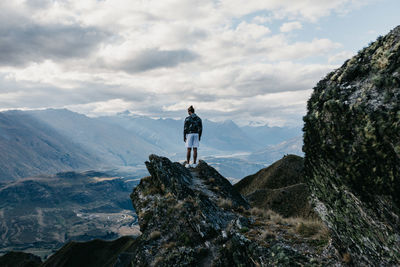 Rear view of man standing on mountain against sky