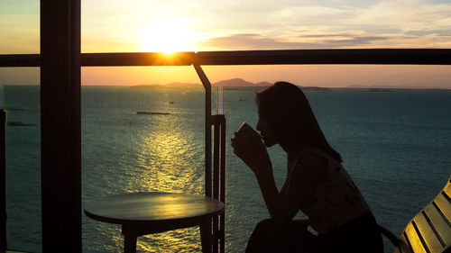 Silhouette man holding railing against sea during sunset