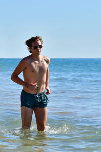 Shirtless man standing at beach against sky