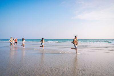 Friends running at beach against sky