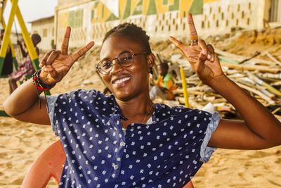 Portrait of smiling young woman showing peace sign while sitting at beach