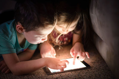 Close-up of siblings using digital tablet while lying on floor in darkroom