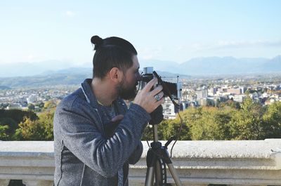 Man photographing by cityscape against sky