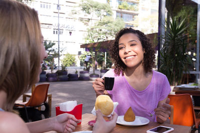 Happy friends enjoying food and drink while sitting at sidewalk cafe