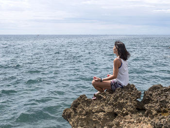 Side view of woman meditation on rock against sea