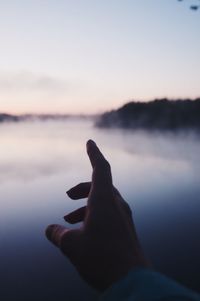 Person hand on lake against sky during sunset