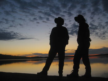 Silhouette couple standing by sea against sky during sunset