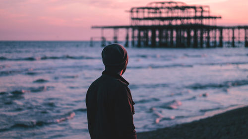 Rear view of man standing against sea during sunset