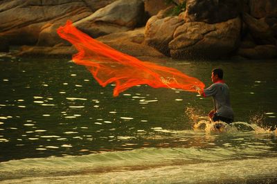 Man throwing fishing net in river against rocks