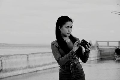 Young woman using mobile phone while standing against sky