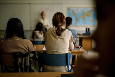 Rear view of teenage girls and boys learning in classroom