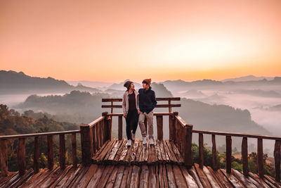 Rear view of men standing on mountain against sky during sunset