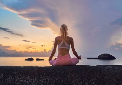 Full length of woman meditating at beach against sky