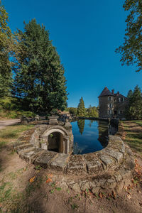 Old building by lake against clear blue sky