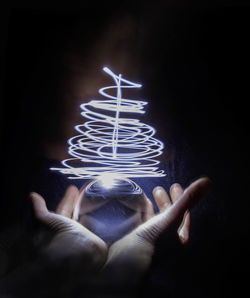 Cropped hand of woman holding illuminated light painting against black background