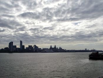 View of buildings by river against cloudy sky