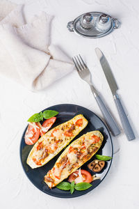 Ready-to-eat baked zucchini halves filled with cheese and tomato and basil leaves and cutlery 