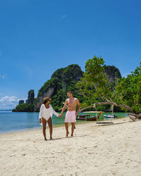 Rear view of friends standing at beach against clear blue sky