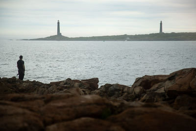 Man standing on rock by sea against sky