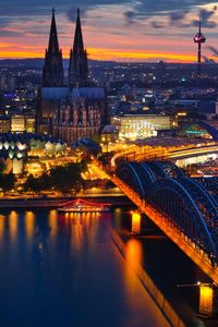 Illuminated bridge over river in city at sunset