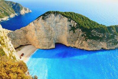 Scenic view of sea by mountain against blue sky