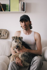 Portrait of man with dog sitting on sofa at home