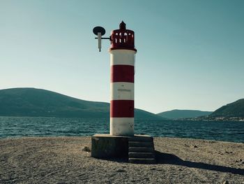 Lighthouse by sea against clear sky