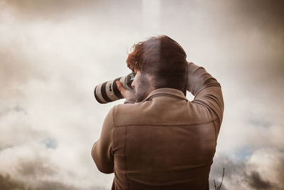 Rear view of man photographing against sky