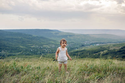 Boy in a beige light overalls walking on the field in the mountains in the summer evening alone