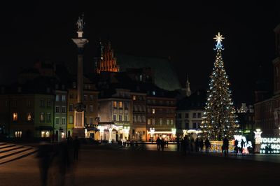 Illuminated christmas tree against buildings in city at night