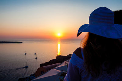 Rear view of woman looking at sea against sky during sunset