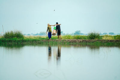 Rear view of two men are carrying each other on the shores of the lake