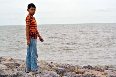 Portrait of boy standing at beach against sky