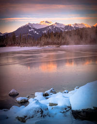 Scenic view of lake by snowcapped mountains against sky during sunset