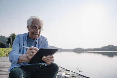Smiling man using digital tablet while sitting on pier