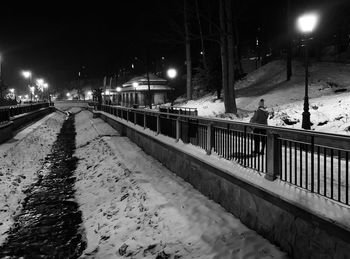 Snow covered footpath by canal in city at night