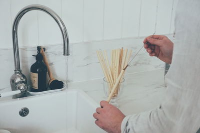 Close up of young man washing reusable bamboo straw at the kitchen sink