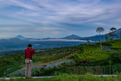 Rear view of man standing on field against sky
