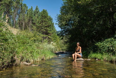 Woman sitting by lake against trees