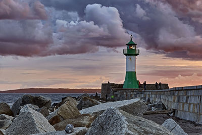 Lighthouse by sea against sky during sunset
