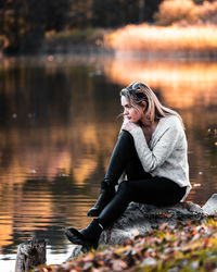 Young woman sitting by lake during autumn