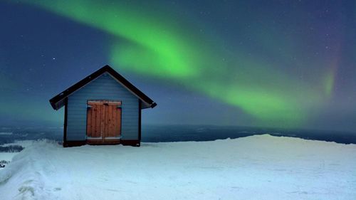 House on snow landscape against northern lights