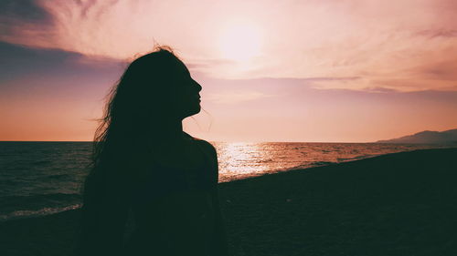 Woman standing at beach against sky during sunset